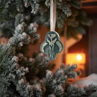 Mini Mythosaur Crest ornament hanging on a snowy Christmas tree branch with warm holiday lights