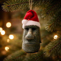 handmade tiki moai ornament with red santa hat hanging from a substantial christmas tree branch