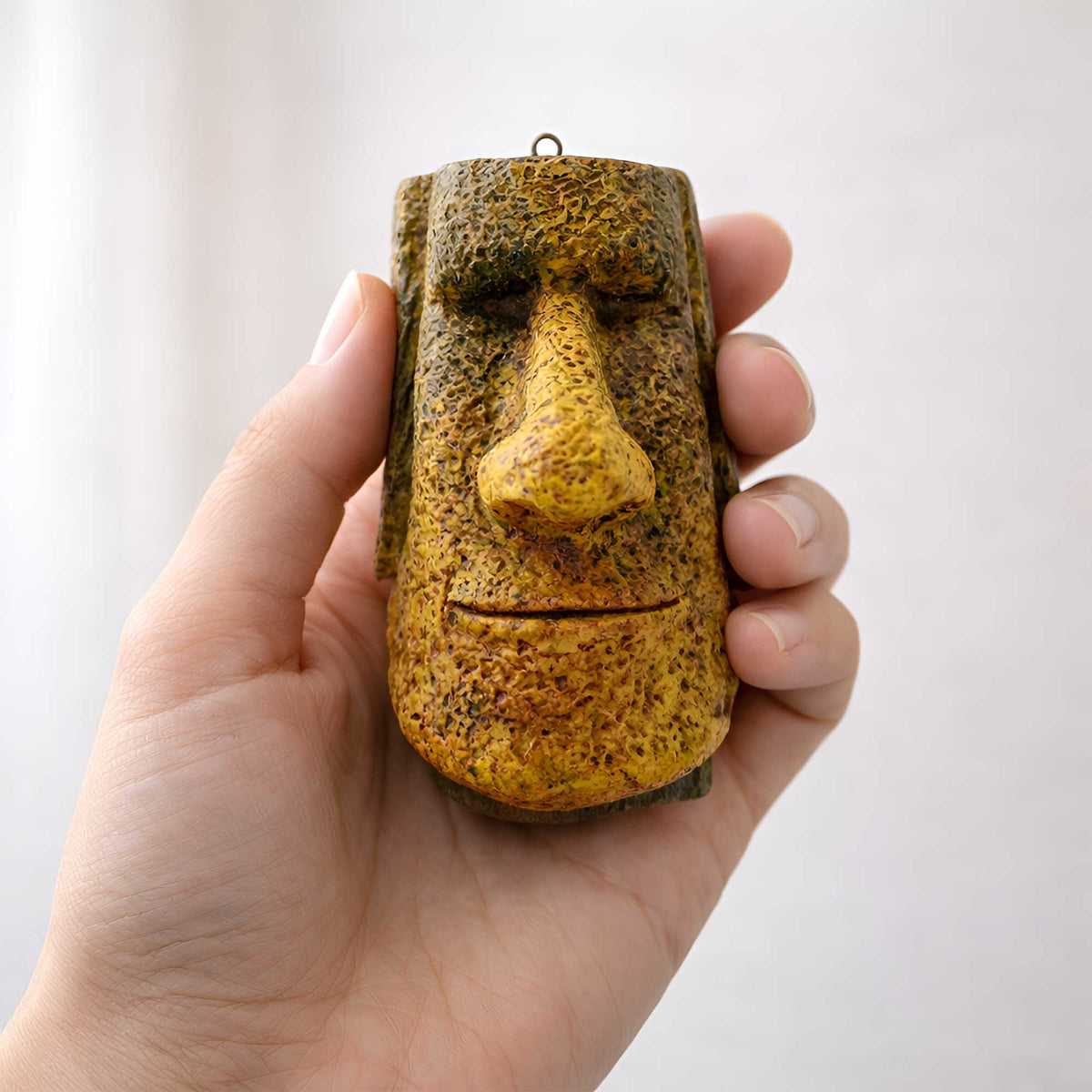 handmade gold tiki moai ornament held in a hand for scale
