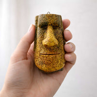 handmade gold tiki moai ornament held in a hand for scale