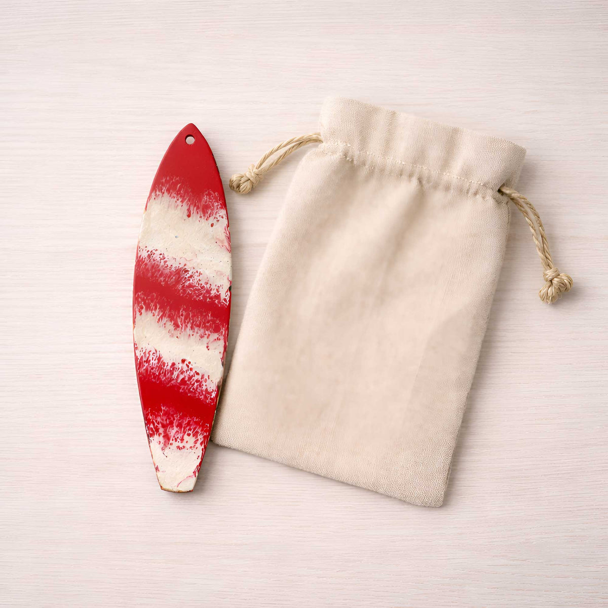 hand painted candy-cane-style surfboard ornament beside an unbranded canvas gift bag
