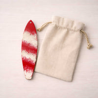 hand painted candy-cane-style surfboard ornament beside an unbranded canvas gift bag