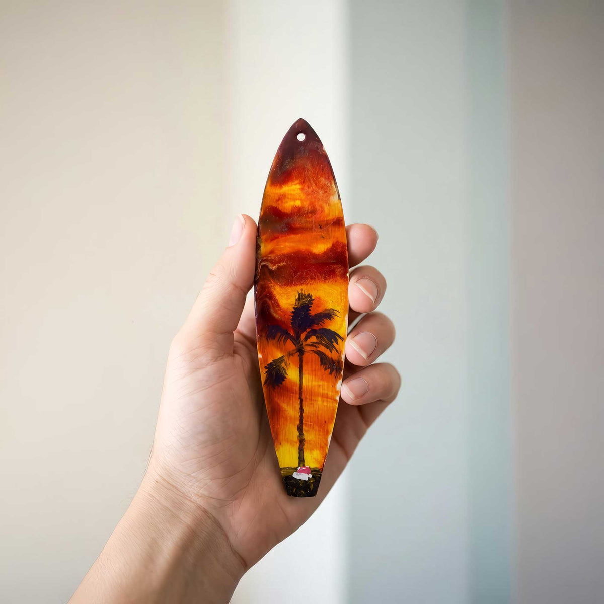 santa’s getaway surfboard ornament shown in hand for size reference