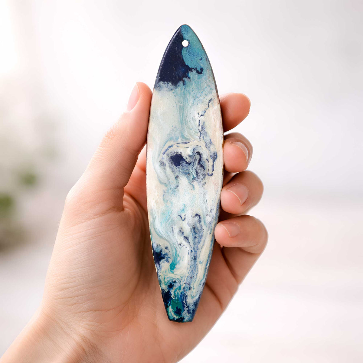 A sea spray surfboard holiday ornament held in hand for scale
