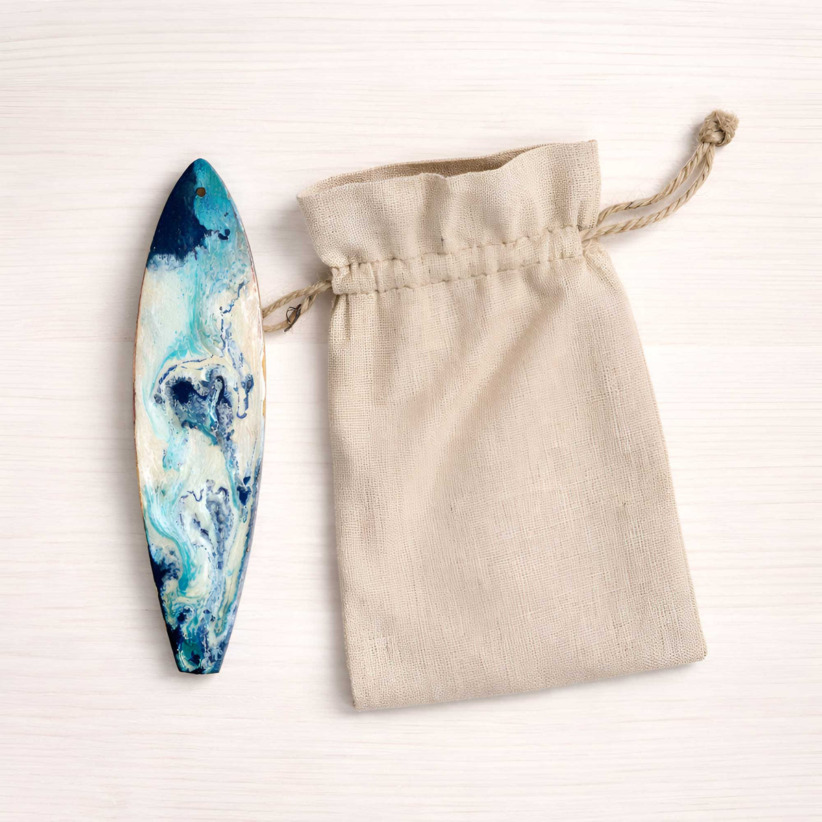 Sea Spray surfboard holiday ornament beside unbranded cotton canvas drawstring gift bag