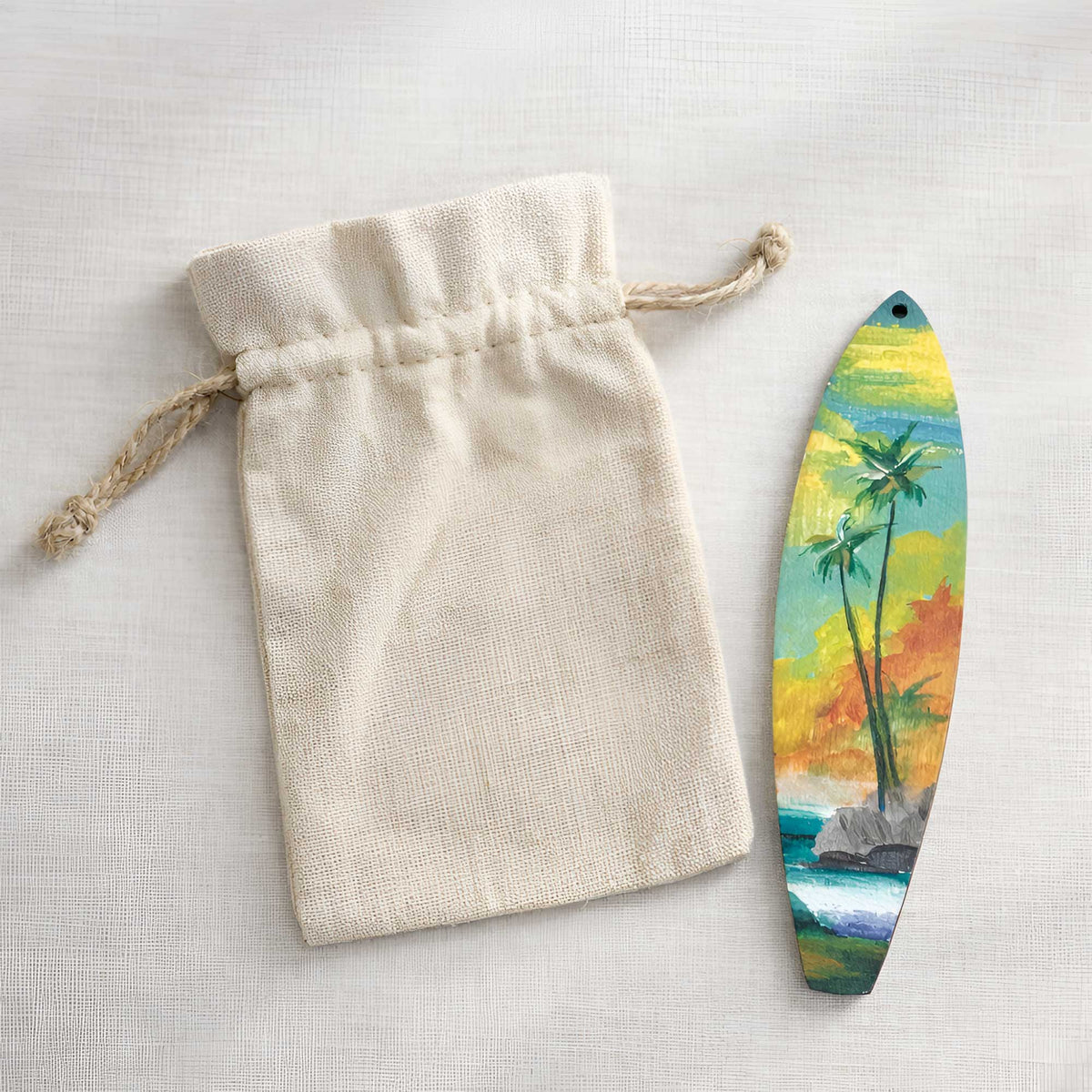 Hawaiian Holiday surfboard ornament displayed beside a natural canvas gift bag, hand-painted with island scenery
