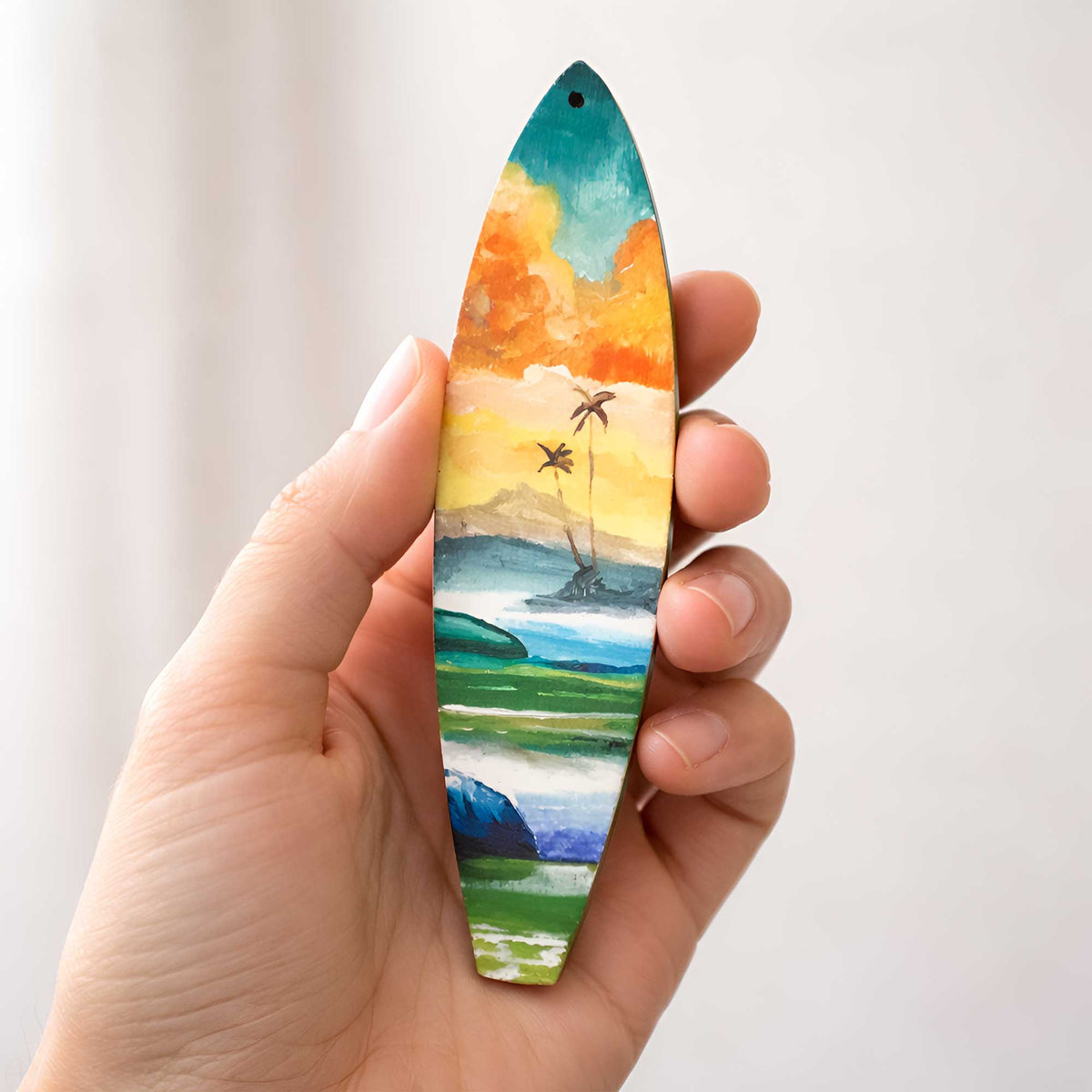 Hand-painted Hawaiian Holiday surfboard ornament held in hand for size reference, featuring tropical island artwork