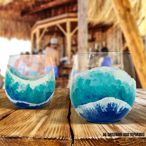Pair of custom glasses for beach wedding with hand-painted ocean waves on stemless red wine glasses by 5th & Rugged. Sitting in a tiki bar on the beach.