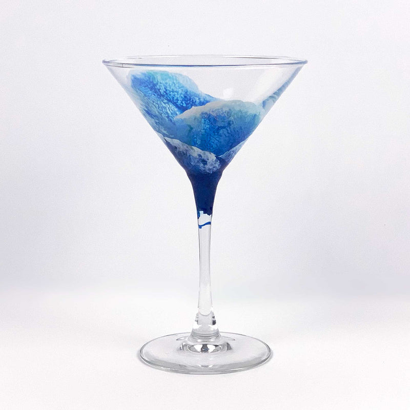 Martini glass hand-painted with blue and white ocean waves, in an abstract and translucent style, wrapping around the clear glass