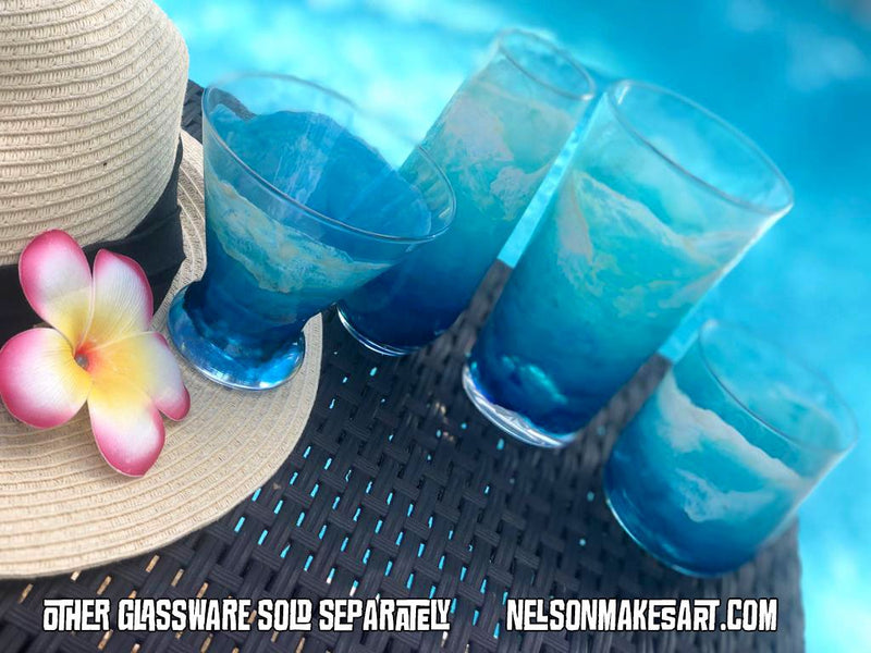 Set of custom coastal glassware painted with surfing waves. Sitting poolside with surfer girl hat and gifts.