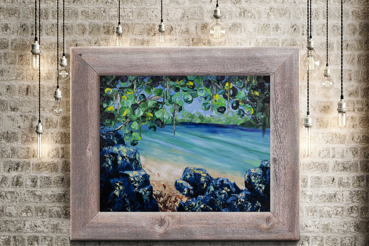 Framed nature wall art of a secluded beach on a clear blue lagoon surrounded by green tropical foliage hanging on a brick wall surrounded by lights.