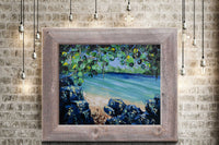 Framed nature wall art of a secluded beach on a clear blue lagoon surrounded by green tropical foliage hanging on a brick wall surrounded by lights.