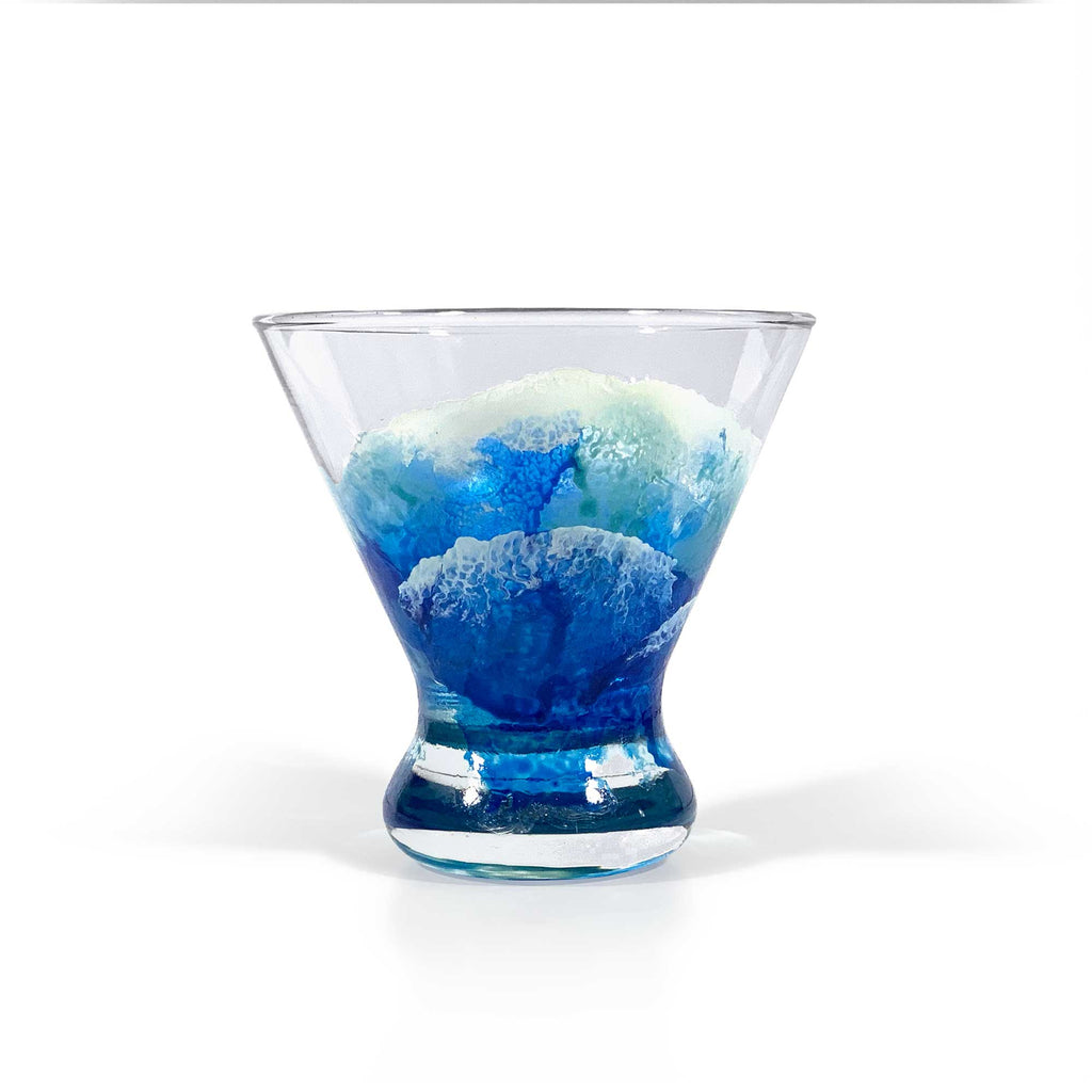 Stemless martini glass hand-painted with blue and white ocean waves, in an abstract and translucent style, wrapping around the clear glass