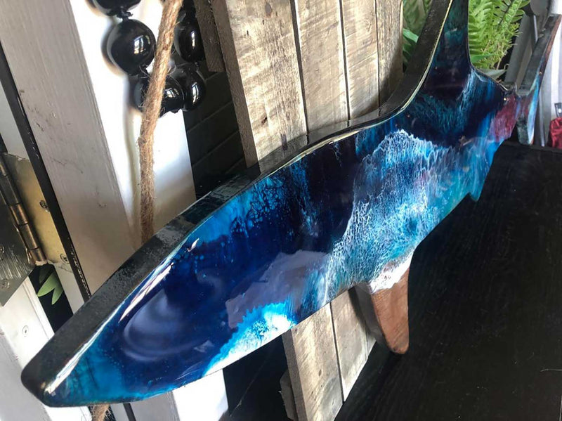 A coastal decor room closeup of a space decorated with a wooden shark painted in blue and green art resin
