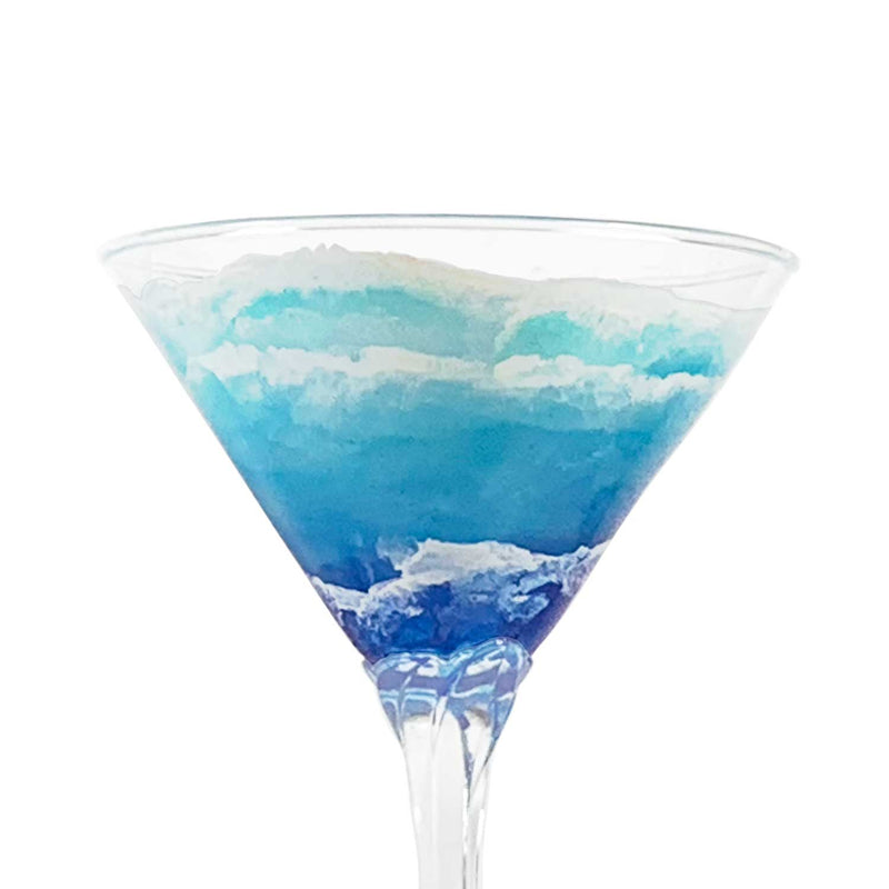 Close view of custom martini glass with blue and aqua hand-painted waves rolling up the shore. Beautiful coastal barware for tiki bar or beach house.