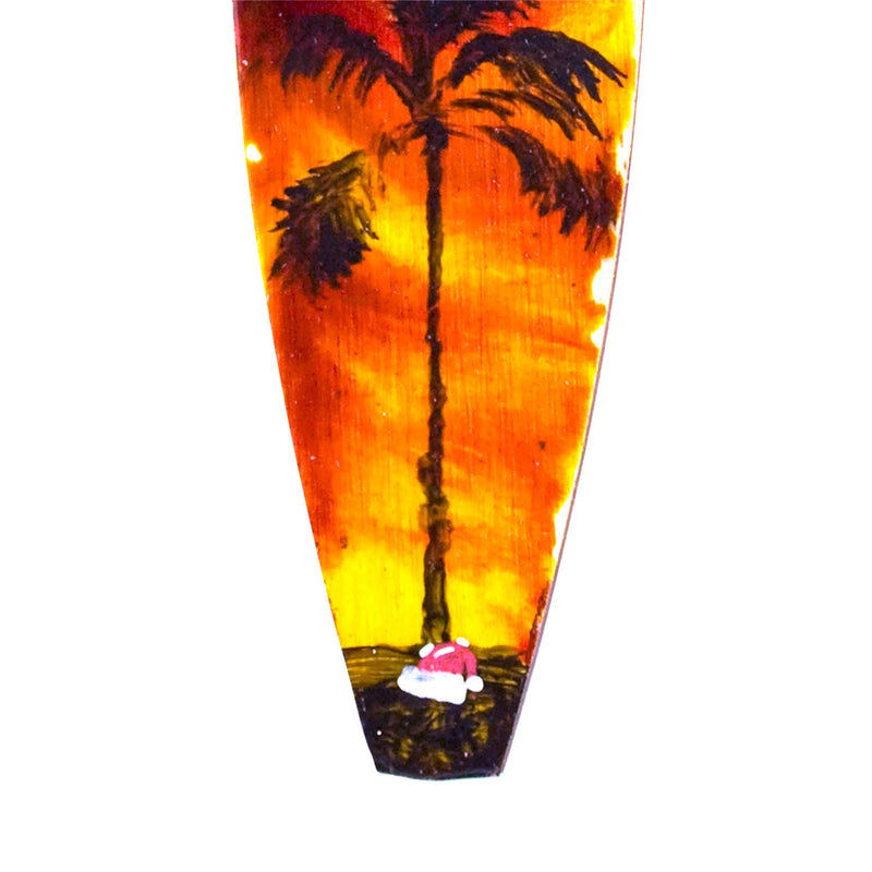 Surfing Santa decoraton with Santa hat on a surfing beach beneath a tropical island palm tree.