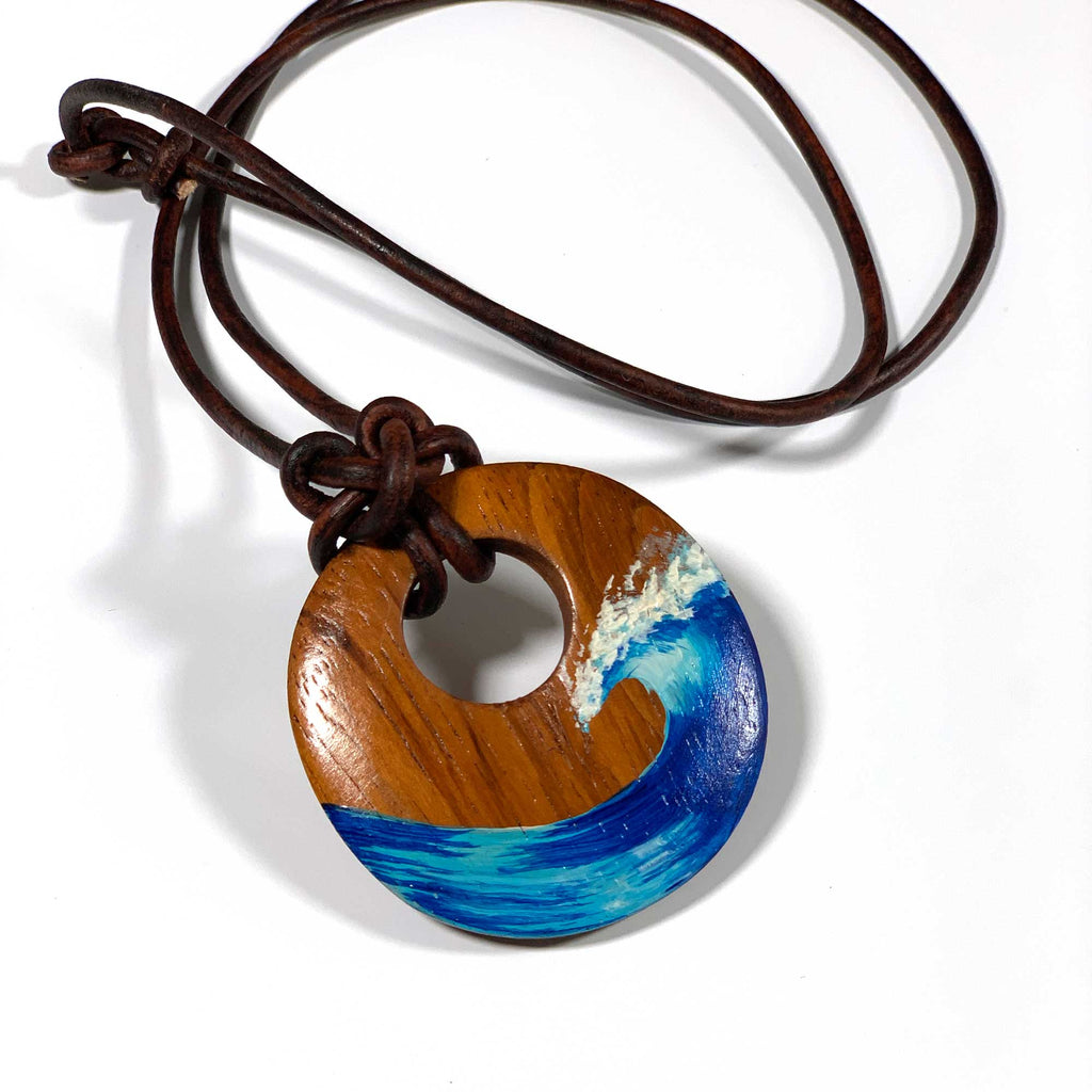 Circular wood pendant featuring a hand painted blue ocean wave with a leather cord and cats claw knot
