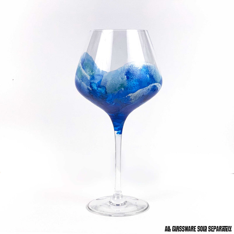 Beach themed glassware of hand-painted surfing waves washing up a red wine glass. Beautiful beach barware, shown from 3 different sides.