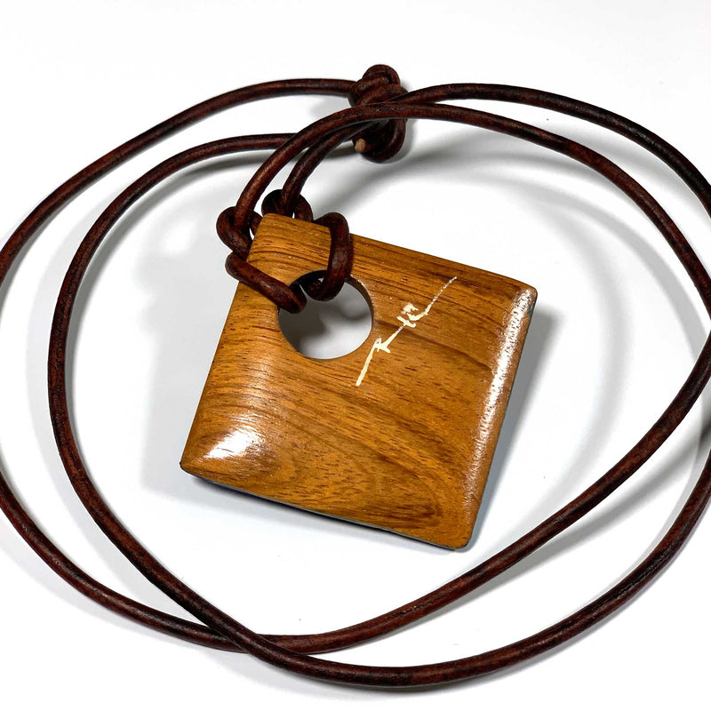Back of a wood pendant necklace with a leather cord necklace, signed by the artist